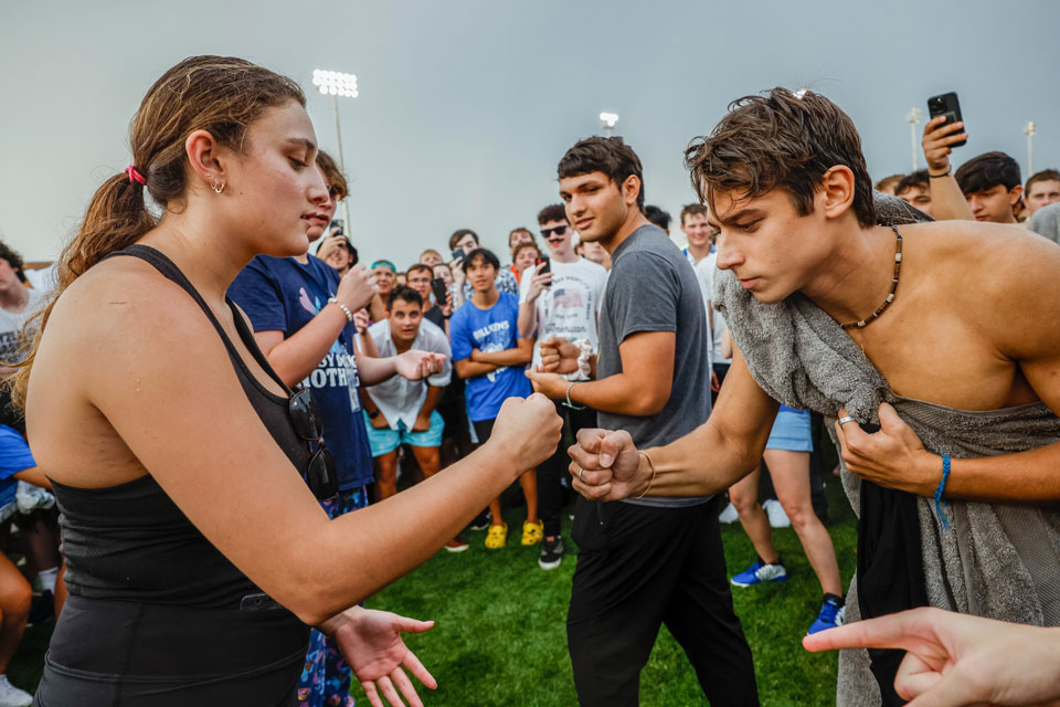 Two students play rock, paper, scissors in front of a crowd