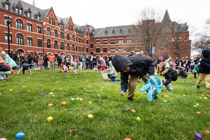 A child in a coat bends down to collect eggs on SLU's quad on an overcast day