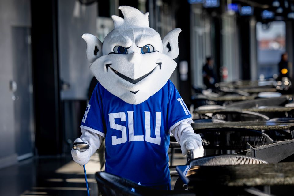SLU Billiken poses with golf clubs for charity event.