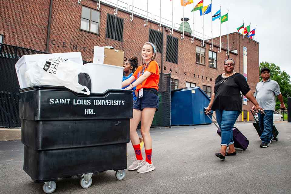 Student helping new SLU family move in, pushing cart to residence hall